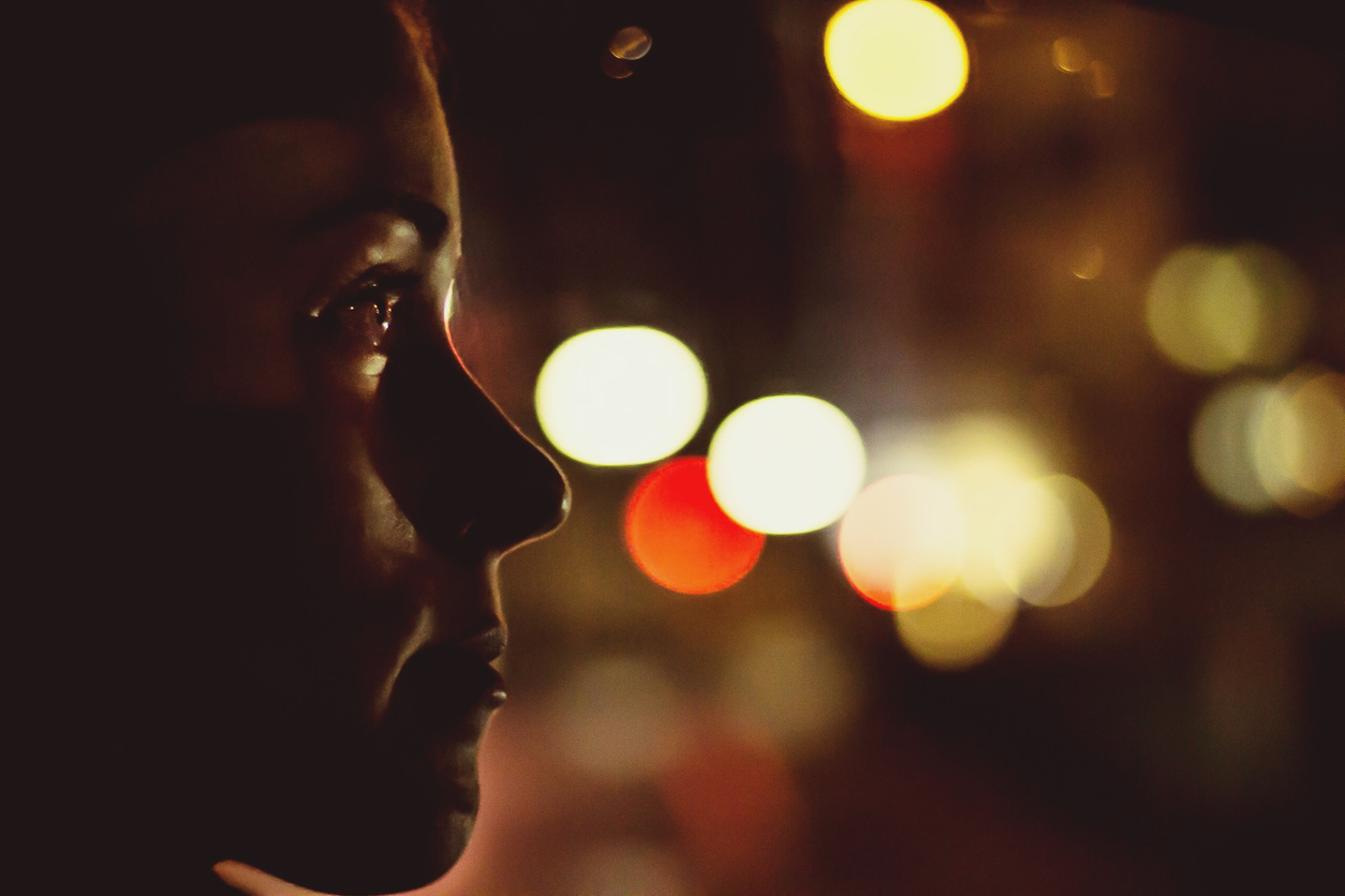 Close-Up Of Woman Looking Away With Illuminated Lights In Background At Night